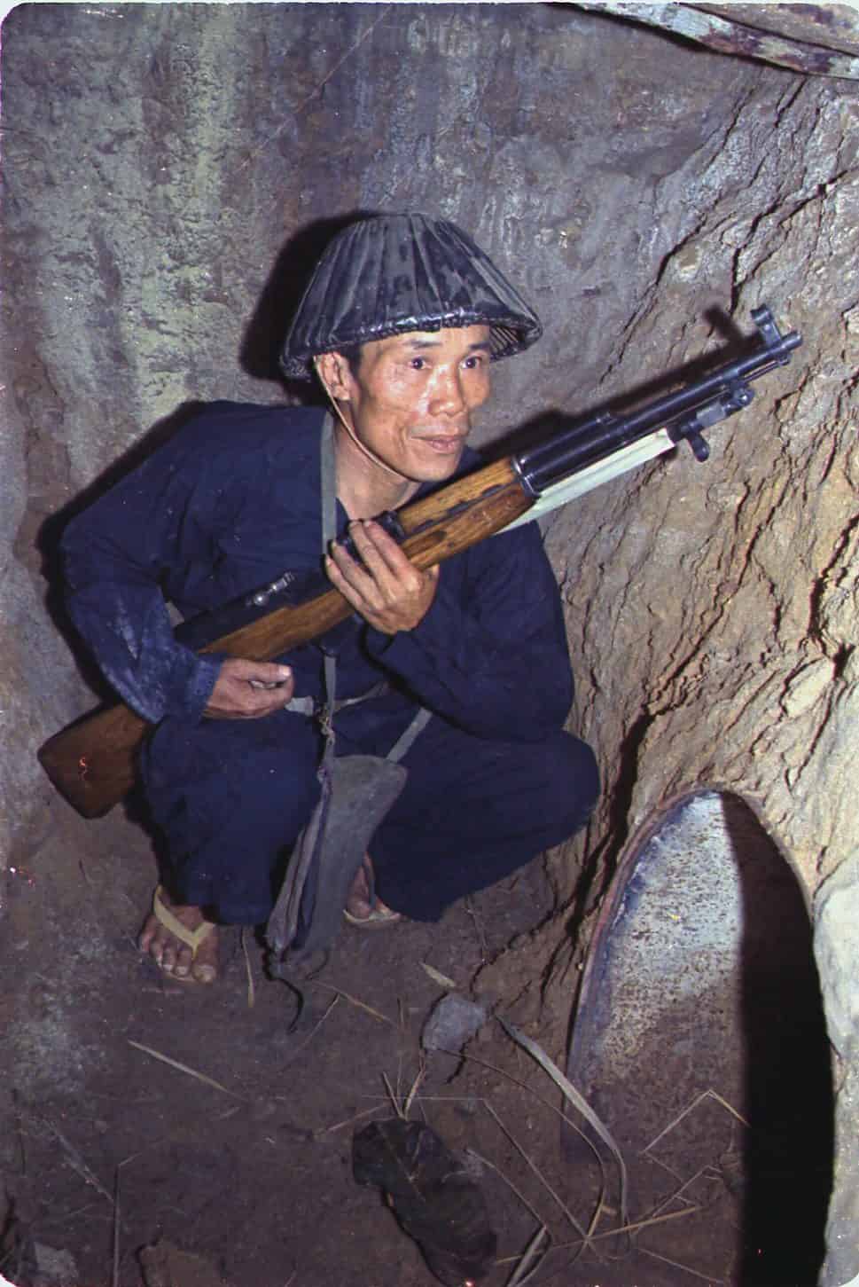 A Viet Cong soldier crouches in a bunker with an SKS rifle. A connecting tunnel is in the foreground