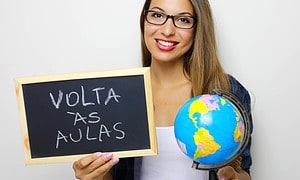 Brazilian Young Female Teacher Holding Globe And Blackboard With Portuguese Written "Volta As Aulas" (Back To School).